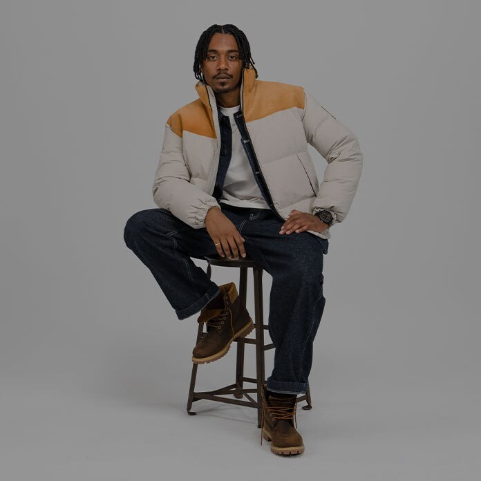 Timberland Holiday Gift Guide image of a man sitting on a stool wearing Timberland apparel and boots