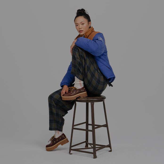 Timberland Holiday Gift Guide image of a woman sitting on a stool wearing Timberland apparel and boots