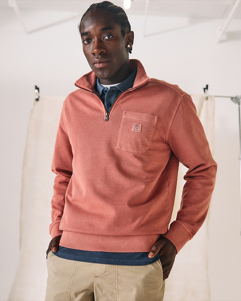 Image of a man looking at the camera wearing a salmon colored Timberland zip up sweatshirt