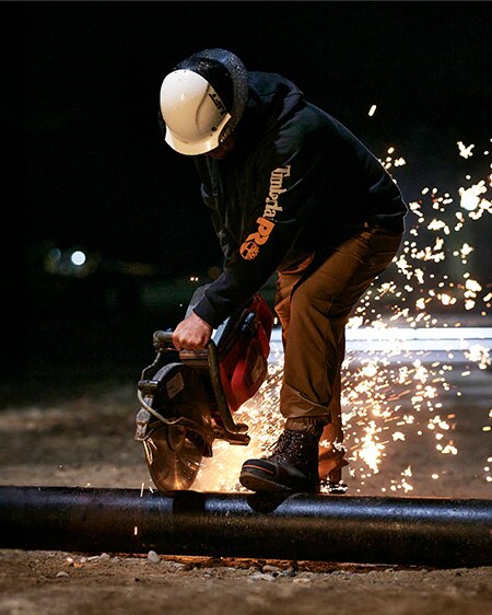 Image of a man wearing Timberland PRO Endurance boots cutting a pipe